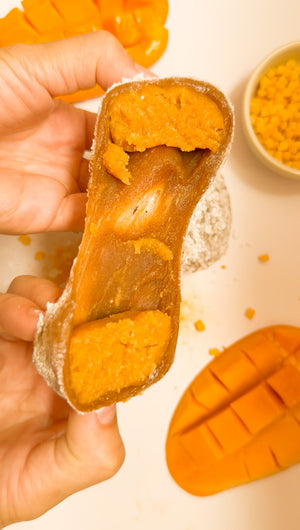 Hands pulling apart a Mango Mookie to reveal chewy mochi and mango filling